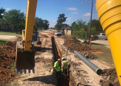 Deep trench in the ground with construction workers inside.